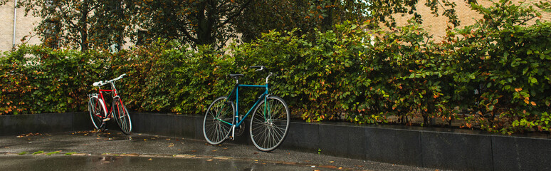 Fototapeta na wymiar Panoramic shot of bicycles near bushes on urban street