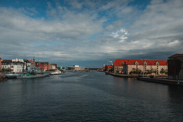 Naklejka premium Buildings near canal and boats in harbor with cloudy sky at background in Copenhagen, Denmark