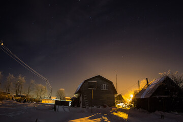 House in the Russian village, winter, snow at night, and the sky a lot of stars. The moon rises behind the house