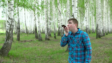 A young man is looking for a cellular network in a birch forest. A man is talking on the phone, but the connection is interrupted. The man is nervous.