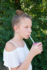 girl drinks fruit juice through a straw in summer park