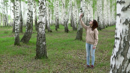 A young woman is looking for a cellular network in a birch forest. A girl is talking on the phone, but the connection is interrupted. The woman is nervous.