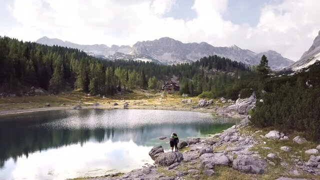 Aerial shot of couple man and woman standing on a rock looking pointing towards mountains next to lake, Triglav National Park, Slovenia