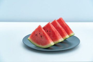 Several pieces of watermelon are placed in a dark blue porcelain dish. A plate of watermelon on a white desktop