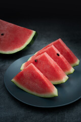 Several pieces of watermelon are placed in a dark blue porcelain dish. Watermelon on dark background
