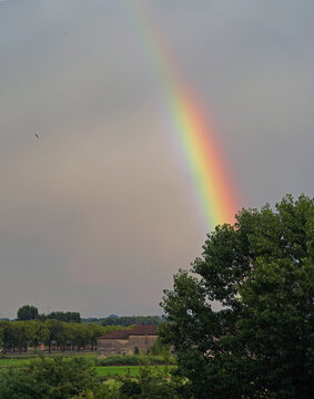 Vercelli, Italy - 06022020: A rainbow stands out toward the sky after a heavy storm. In the background, a farmhouse and a rice field
