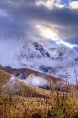 Emotional, dramatic sunrise over snow-capped mountain peaks and a meadow with dried grass