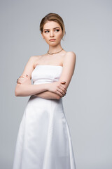 displeased bride in white wedding dress standing with crossed arms isolated on grey