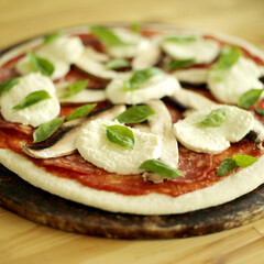Raw pizza base with basil and mozzarella topping