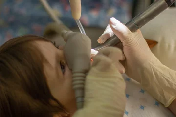 Foto op Canvas een dokter behandelt een melktand aan een meisje in een tandheelkundige kliniek © Albert Ziganshin