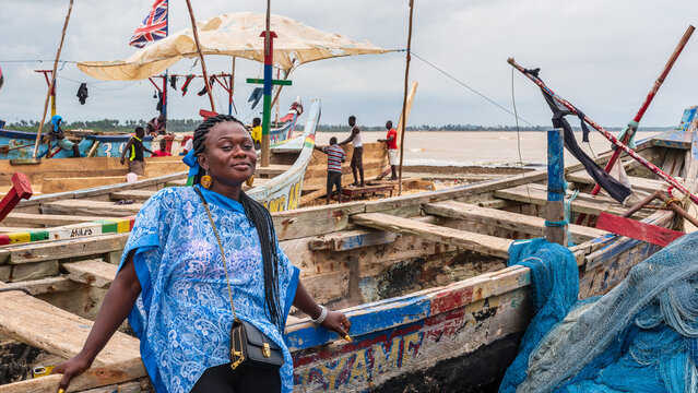 African woman from Ghana with blue dress stands by a fishing boat in fishing village Shama Ghana West Africa 2019 September 15