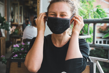 New normal fashion look, a very happy young Caucasian girl puts on black medical protection face...
