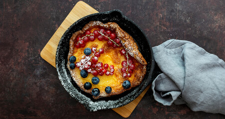 Top view of Dutch or german baby pancake in skillet iron pan with red currant, blueberry, and sugar powder. Close up.