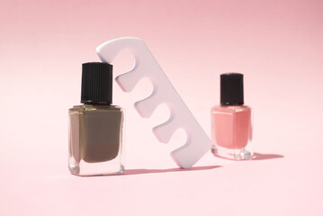 Nail polish bottles and pedicure sponge separator on pink background with copy space, vertical. Beauty product for manicure. Concept nail care in minimalist style for branding