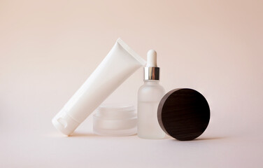 Body lotion in white plastic tube, open moisturizer cream in glass jar and liquid serum with...