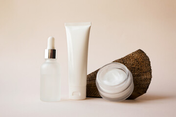 Serum dropper, body lotion on tube and open moisturizer cream in white glass jar and textured...