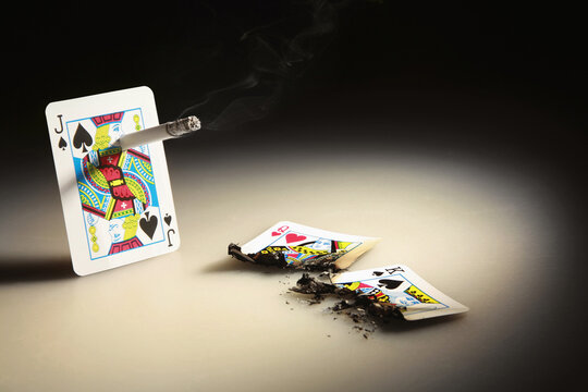 Jack of spades playing card smoking cigarette, two other burnt playing cards by the side