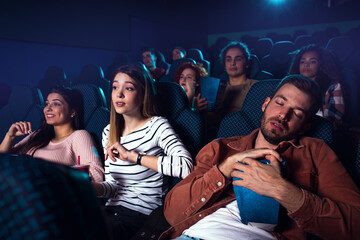 Group of  people watching movie in cinema, girl wakes the sleeping boyfriend.
