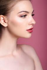 nude and young woman with makeup looking away on pink