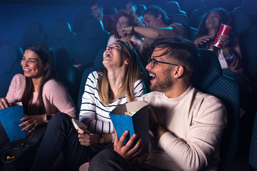 Group of cheerful people laughing while watching movie in cinema.