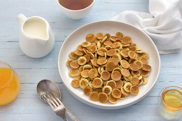 Plate of Mini Pancakes cereals with honey, cream and fresh orange juice on a light blue background. trendy food. homemade breakfast. top view