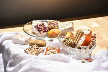 Still life of Lebanese sweets (made from honeyed orange paste, dried fruits, roasted almonds, pistachios and rose petals) on a recycled wooden table covered with a white cloth. Chiaroscuro