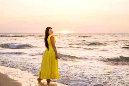 Girl in a yellow dress meets dawn on the seashore
