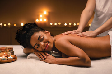 Obraz na płótnie Canvas African american woman enjoying romantic atmosphere during body massage