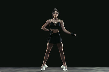 Fototapeta na wymiar Beautiful young female athlete practicing on black studio background, full length portrait. Sportive fit brunette model posing confident. Body building, healthy lifestyle, beauty and action concept.