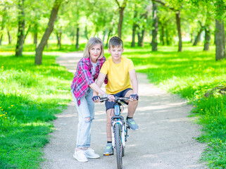 Happy family. Sporty family leisure. Mom teaches her young son ride a bike in summer park. Empty space for text