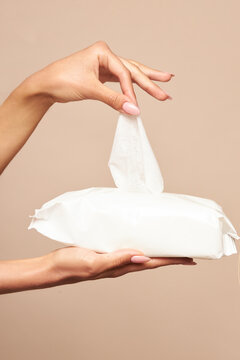 Hygiene. Female hands takes wet wipes from white packaging on a beige background. Daily hygiene for the prevention of viral and bacterial infections.