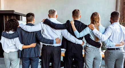 Business Team Embracing Standing Back To Camera In Office, Panorama