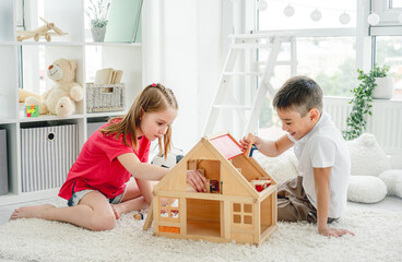 Cute little boy and girl playing with wooden doll house indoors