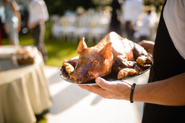 The waiter serves the roast pig on an oval at an outdoor party