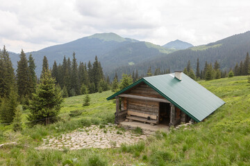 Fototapeta na wymiar Mountain hut on a green meadow with spruce forest. Mount Berlebashka, Carpathians, Marmaroshchyna, Maramures, Ukraine