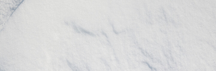 Beautiful winter background with snowy ground. Natural snow texture. Wind sculpted patterns on snow surface. Wide panoramic texture for background and design. Closeup top view with copy space.