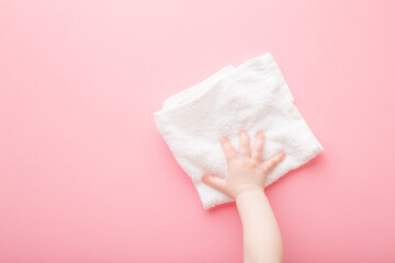 Baby hand wiping light pink table or wall surface from dust with white dry rag. Closeup. Point of view shot. Regular cleanup in nursery room. Top down view.