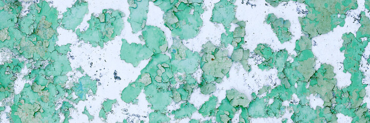 Peeling paint on the wall. Panorama of a concrete wall with old cracked flaking paint. Weathered rough painted surface with patterns of cracks and peeling. Wide panoramic grunge texture for background