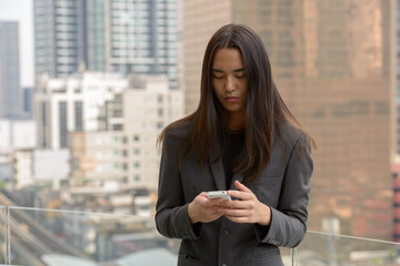 Fototapeta premium Young Asian businessman with long hair using phone in the city outdoors