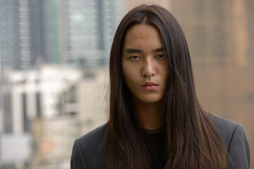 Face of young Asian businessman with long hair in the city outdoors