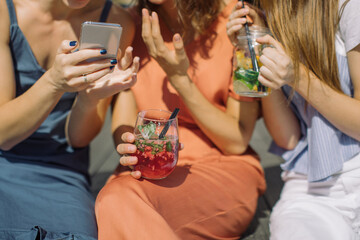 Girls sitting on summer terrace in the city, drinking lemonade, talking and looking at mobile phone screen.