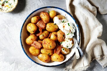 Baked young potatoes with bacon and sour cream sauce on a gray background, still life