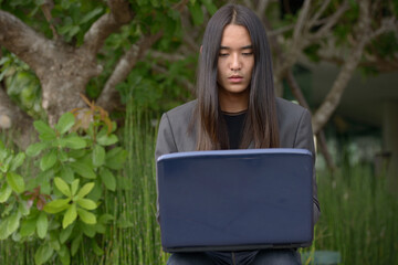 Young Asian businessman with long hair using laptop at the park