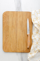 Vertical image.Top view of wooden cutting board,knife and napkin on the white marble table