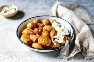 Baked young potatoes with bacon and sour cream sauce on a gray background, still life