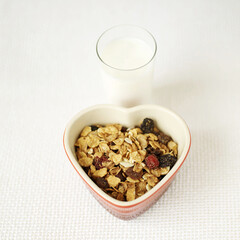 Muesli in heart bowl with a glass of milk