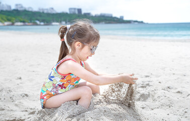 Little cute girl playing in the sand on the beach by the sea