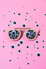 Psychedelic and surreal plastic glasses with lots of eyes and among of another cartoon eyes on pink pop art background.