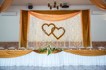 Beautiful golden brown and white decoration for wedding ceremony or banquet decoration. On the table is a large bouquet of flowers and white silk. Two hearts in the background. Lover's Day.