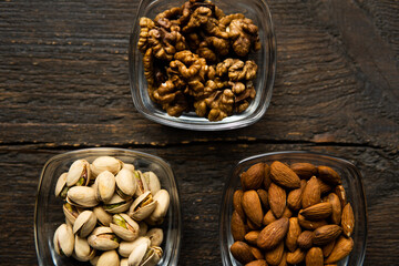 Almond, pistachio and walnut in a small plates which standing on a vintage wooden table. Nuts is a healthy vegetarian protein and nutritious food.